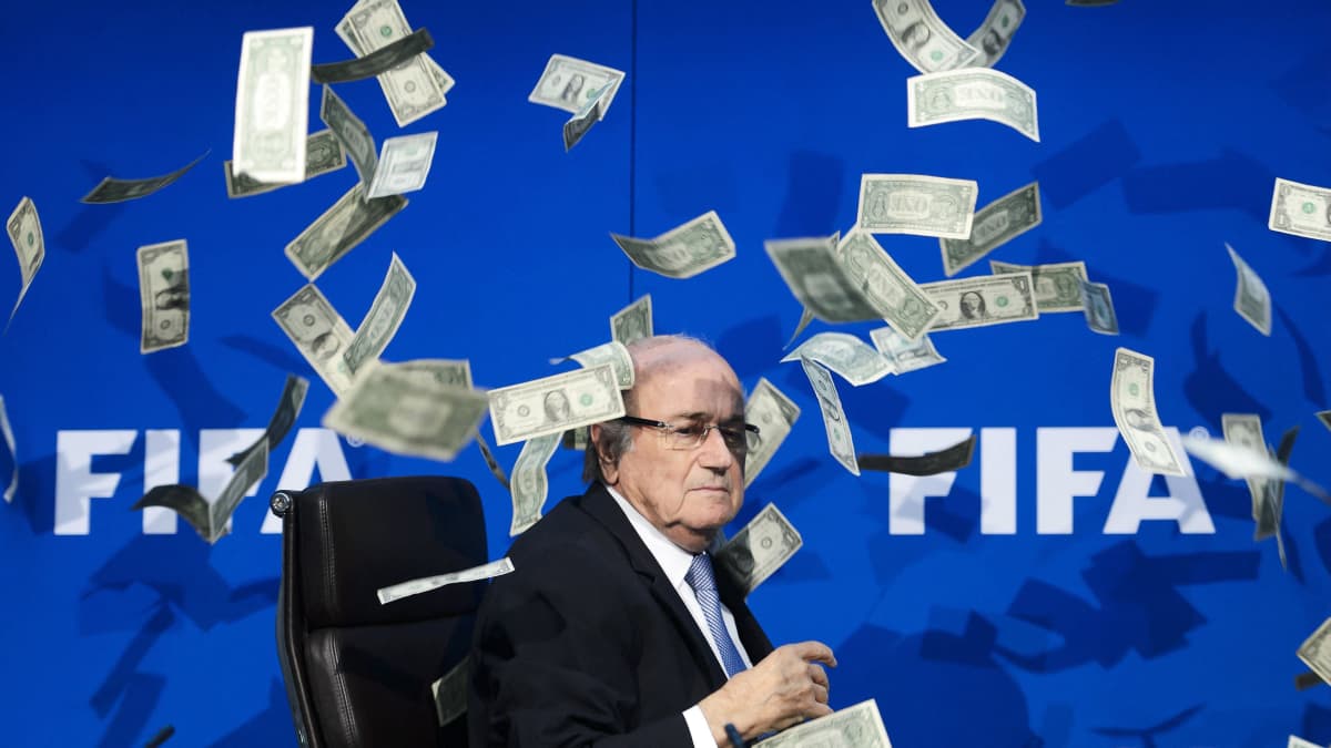 Kansainvälisen jalkapalloliiton puheenjohtaja Sepp Blatter istuu lehdistötilaisuudessa. Hänen ympärillään leijailee väärennöksiä Yhdysvaltain dollareista, jotka tilaisuuteen saapunut brittikoomikko heitti ilmaan kritisoidakseen Fifan korruptiota. Kuva on vuodelta 2015 Sveitsistä.