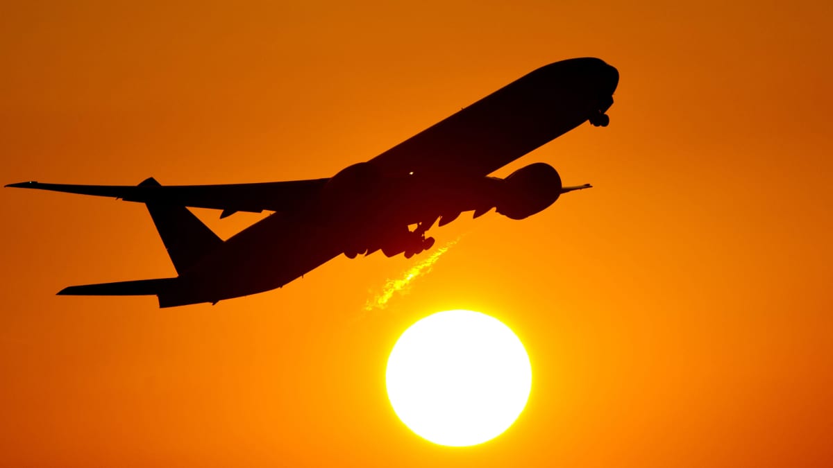 Lentokone nousee taivaalle oranssinkeltaista taivasta ja aurinkoa vasten.