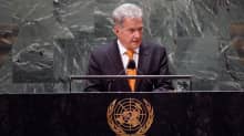Niinistö, wearing a dark suit and orange tie, speaks at a podium behind the UN logo.