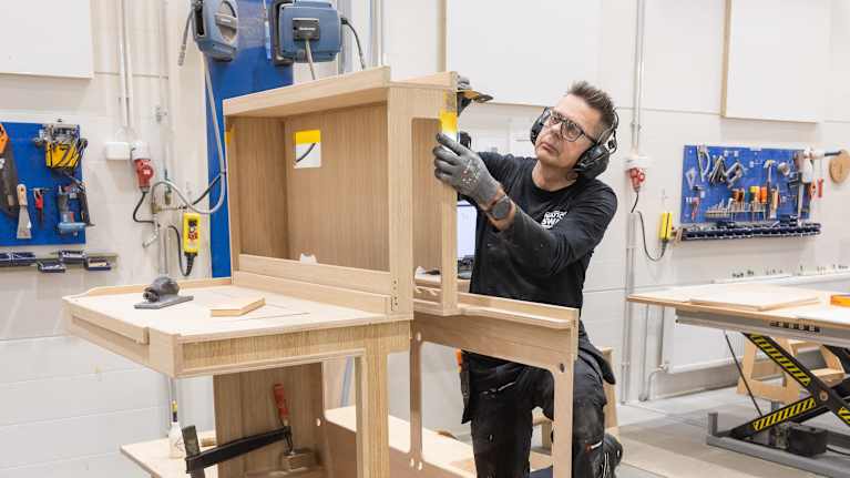 En person arbetar med att montera en trästruktur i en verkstad.