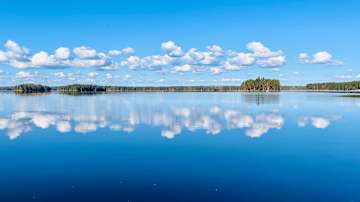 Suomen kesäinen järvimaisema heijastuu tyynessä vedessä.