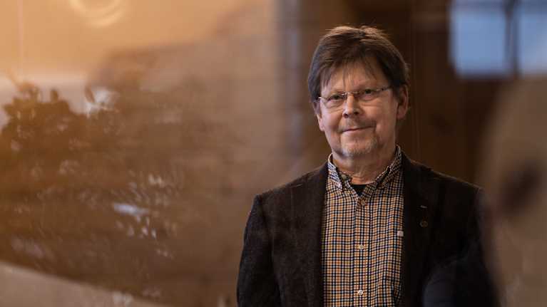 En man i mörk kavaj tittar mot kameran genom ett fönster