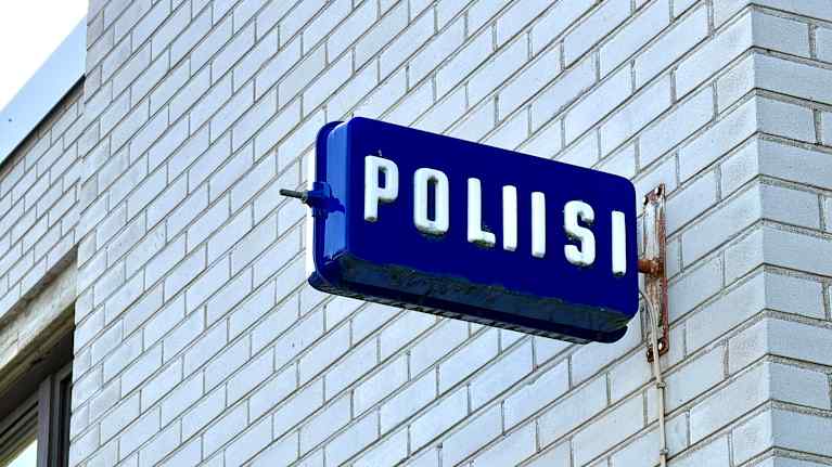 Kangasalan poliisiaseman valkoisen tiilirakennuksen sivu. Seinässä on sininen poliisikyltti.