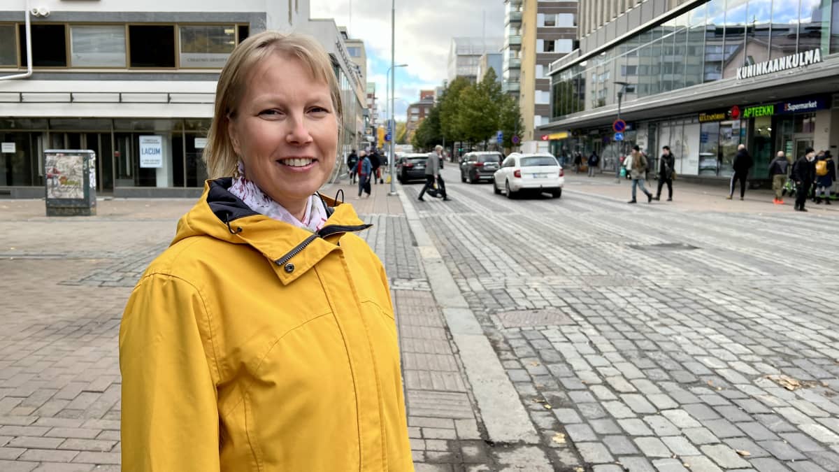 Keltaiseen takkiin pukeutunut Katja Seimelä seisoo kadulla ja katsoo kohti kameraa.