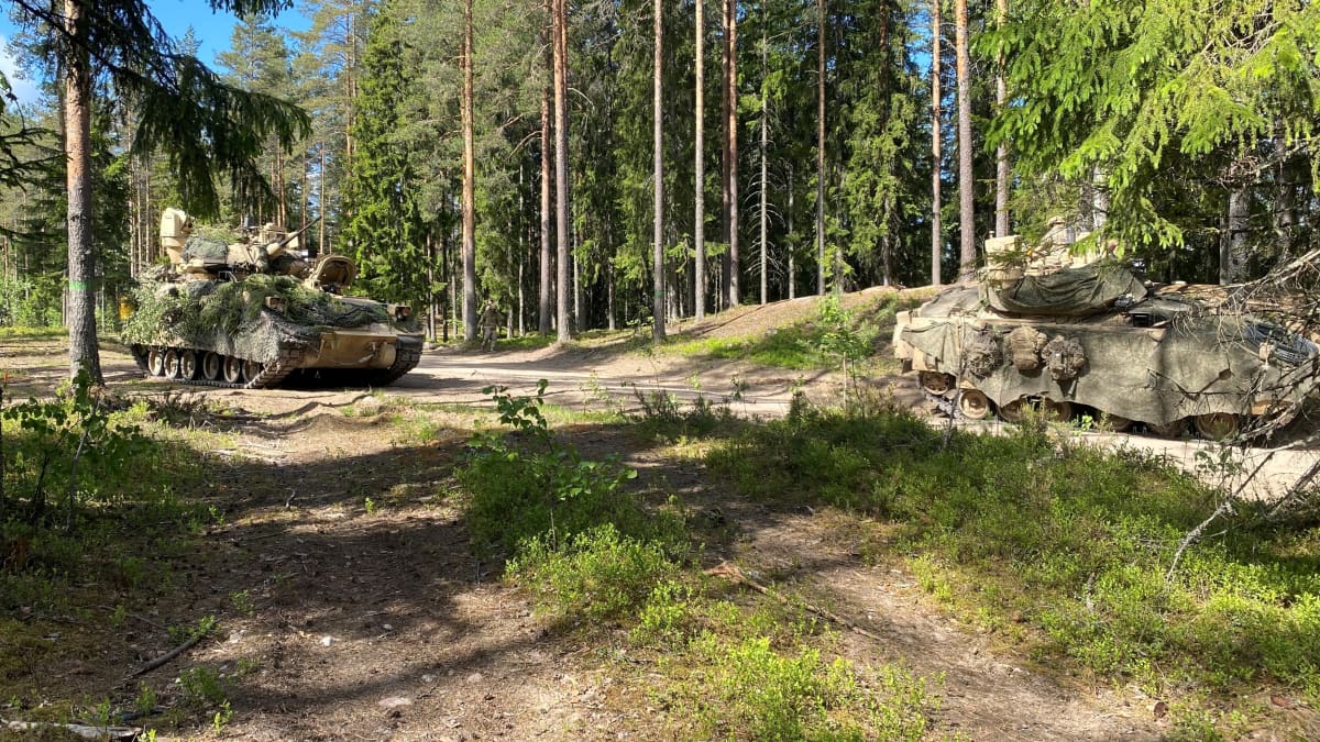 Kaksi maastoon naamioitua panssarivaunua ajaa metsäautotiellä.