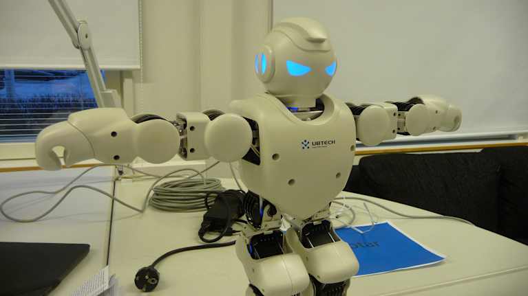 En robot står på ett bord med händerna utsträckta.
