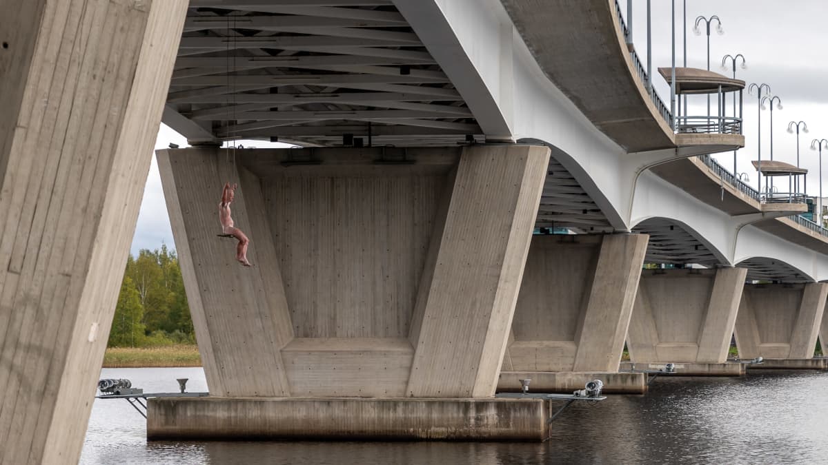 Keinuja taideteos, jossa lasikuidusta tehty ihminen istuu keinussa Kuokkalan sillan alla.