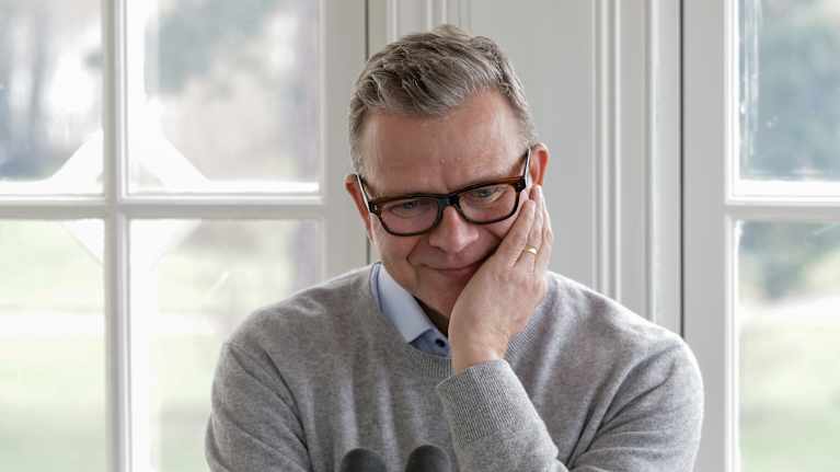 A middle-aged man in glasses rests his face in his hand.