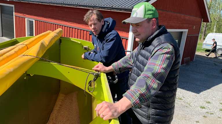 Två mån står böjda över ett lantbruksredakap på en gårdsplan