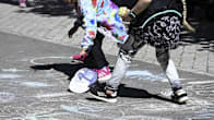 Two children in summer clothes playing on pavement with colourful chalk marks, with their heads cropped out of the picture.