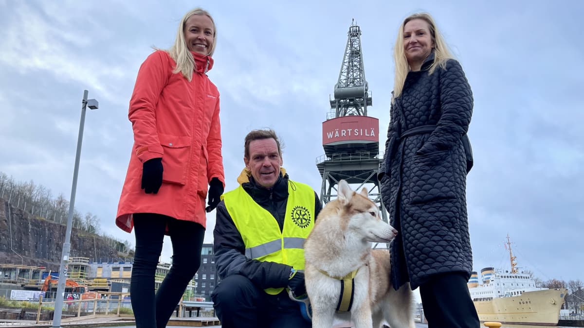 Sini Häkkinen punaisessa takissa, Tommi Sundqvist keltaisessa huomioliivissä ja Marjo Malin musta takki yllään Wärtsilän punaisen nosturin edessä.