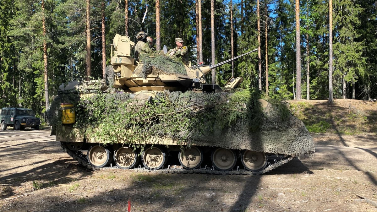 Panssarivaunu ajaa metsätietä. Sen päällä matkustaa useita varusmiehiä.