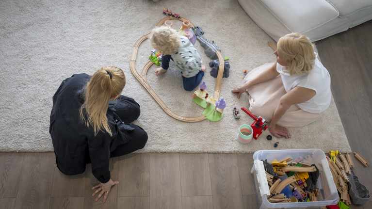 Lapsi leikkii lattialla junaradalla vanhempiensa kanssa.
