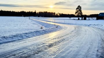 Jäinen kylätie mutkittelee lumisessa maisemassa. 