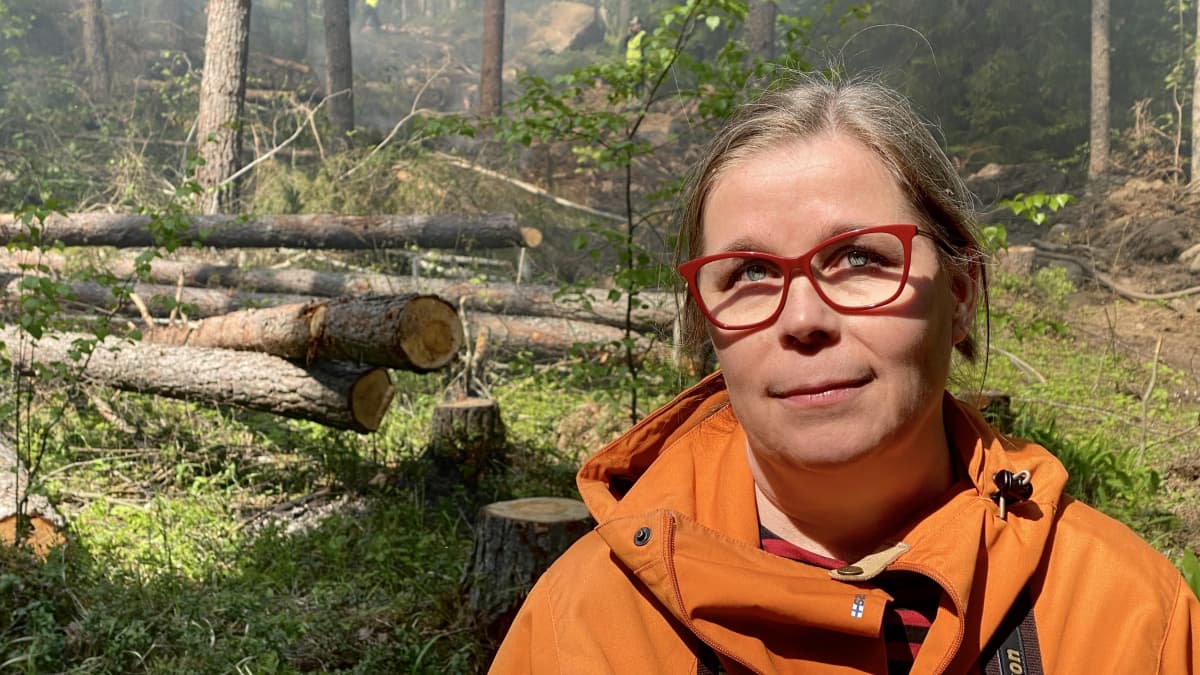 Nainen seisoo hakatun metsän keskellä.