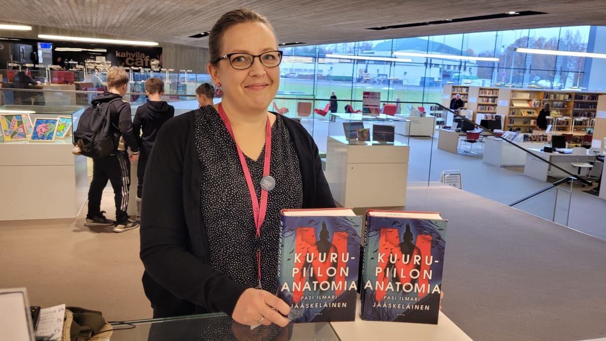 Kirjaston palvelupäällikkö Hanna Kotila pitää esillä kahta Finlandia-palkintoehdokkuuden saanutta kirjaa. Taustalla Seinäjoen kaupunginkirjasto Apilan kirjahyllyjä ja iso ikkuna.