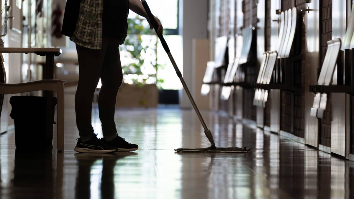 Siivooja moppaa lattiaa käytävällä.