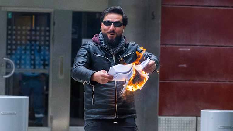 Salwan Mamika se lève et rit alors qu'il brûle un Coran.