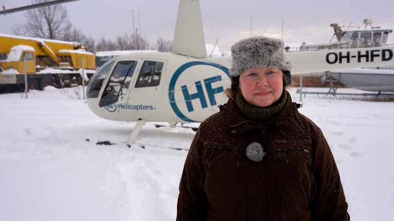 Kvinna står med vinterkläder på framför en helikopter och ser mot kameran.