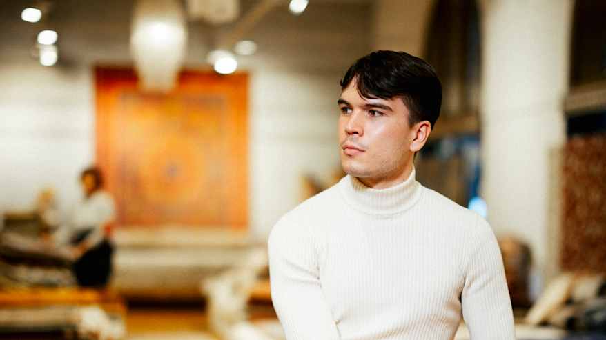 A person dressed in a light sweater is sitting on top of a pile of carpets.