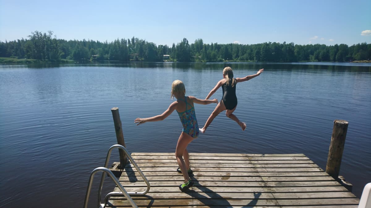 Kaksi tyttöä hyppäämässä laiturilta järveen.