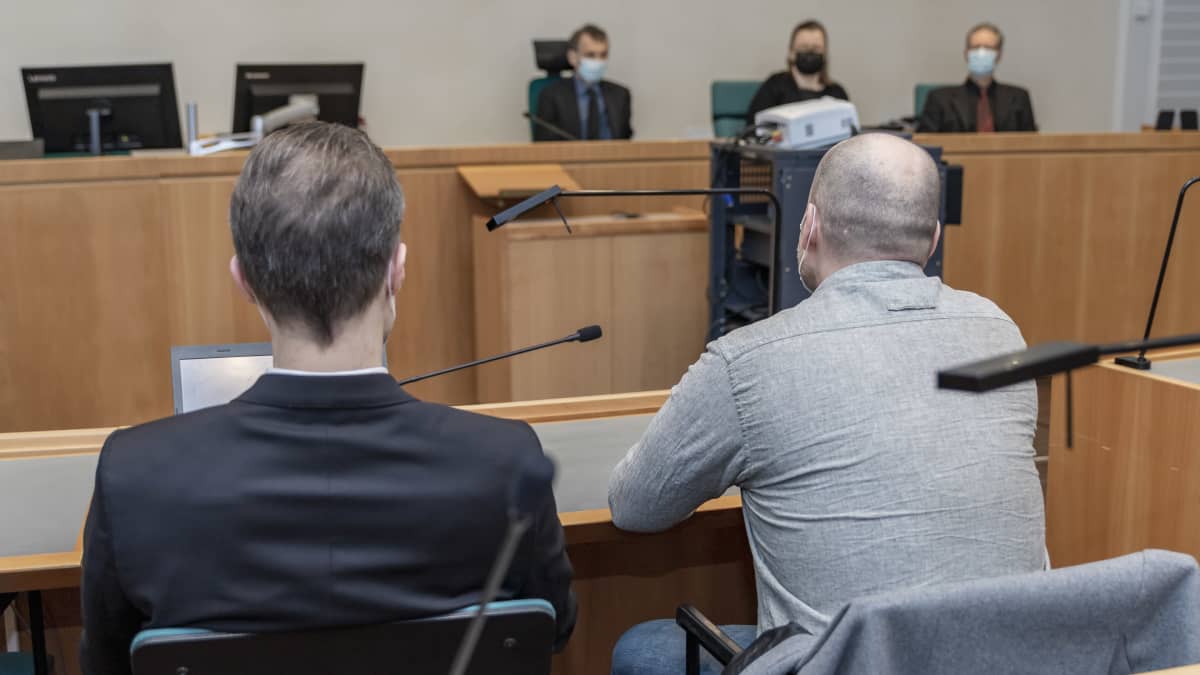 Syytetty istuu asianajajansa kanssa oikeussalissa.