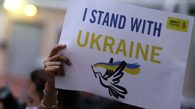 En hand håller upp ett plakat med amestys logo och en fredsduva där det står "I stand with Ukraine".
