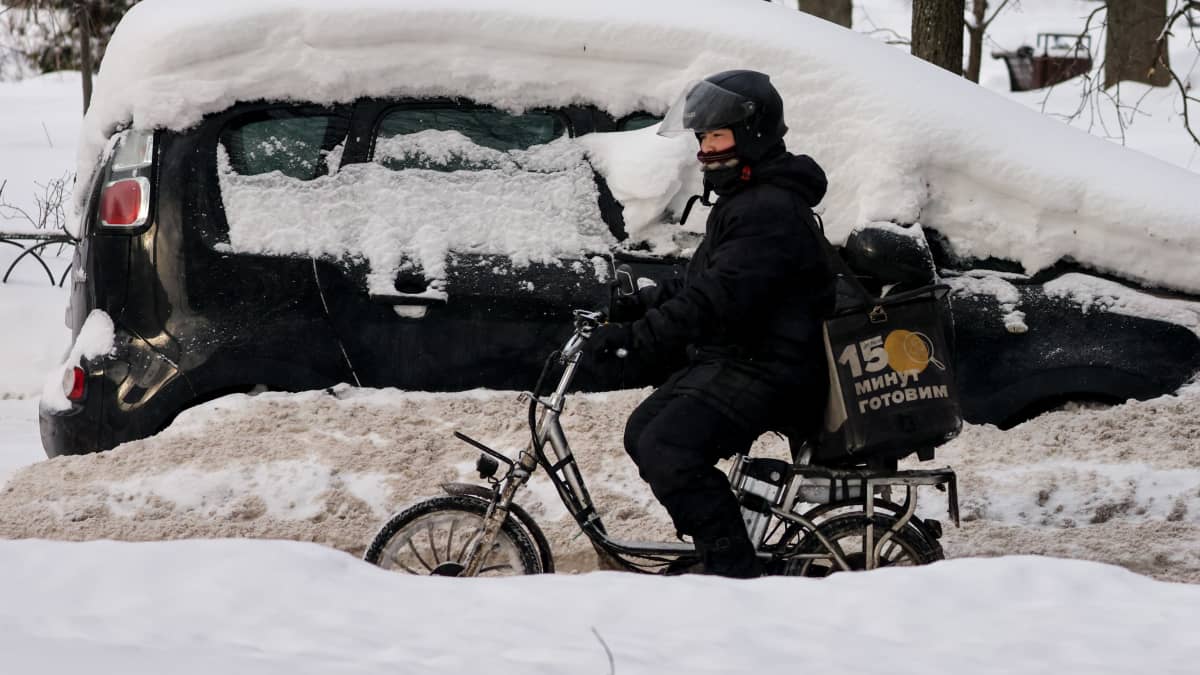 Ruokalähetti pyöräilee lumikinosten keskellä Moskovassa.