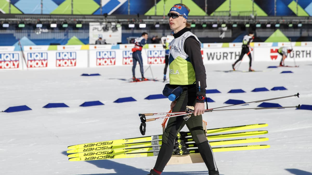 Iivo Niskanen kävelee suksipakan kanssa Planican stadionilla.