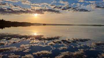 Rauhallinen auringonnousu järvellä, jossa pilvet heijastuvat tyynestä vedenpinnasta.