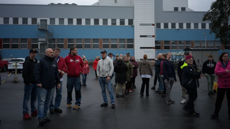 Työntekijät ulosmarssivat työpaikalta ja seisovat ulkona.