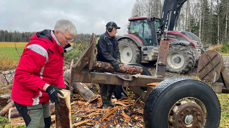En man och en kvinna jobbar med ved intill en traktor ute på en gårdsplan.