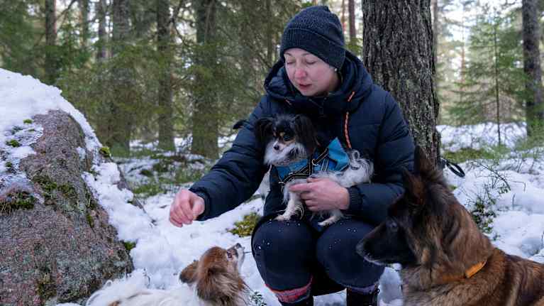 En kvinna med en hund i famnen som sträcker sig för att klappa en annan hund. 