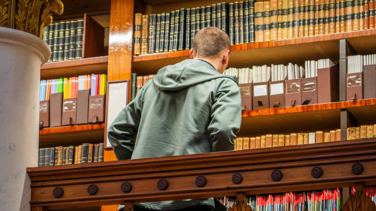 Henkilö katsoo kirjoja kirjahyllyssä Kansalliskirjaston kirjaston parvella.
