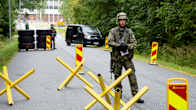 An armed soldier in a green uniform stands on a road amid yellow protective devices.