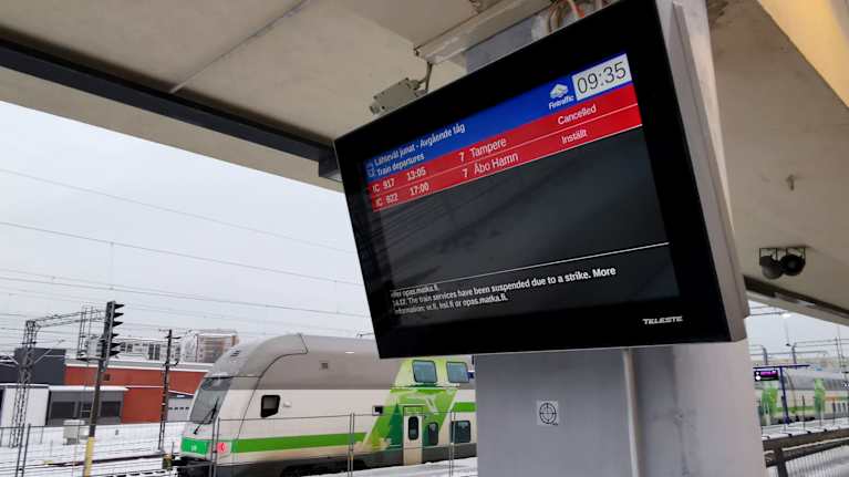 The screen on the train platform showed that two trains were cancelled and a white-green train at the back was parked in the snow.