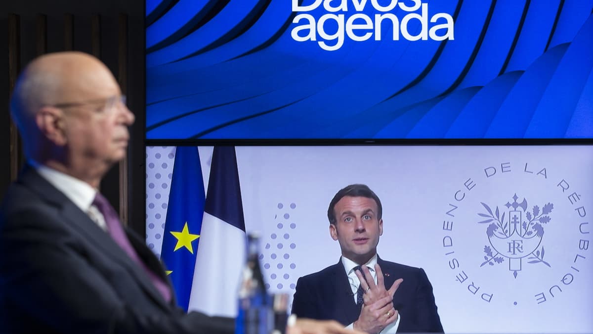 Maailman talousfoorumin puheenjohtaja kuuntelee, kun Ranskan presidentti Emmanuel Macron puhuu ruudulla videokonferenssissa.