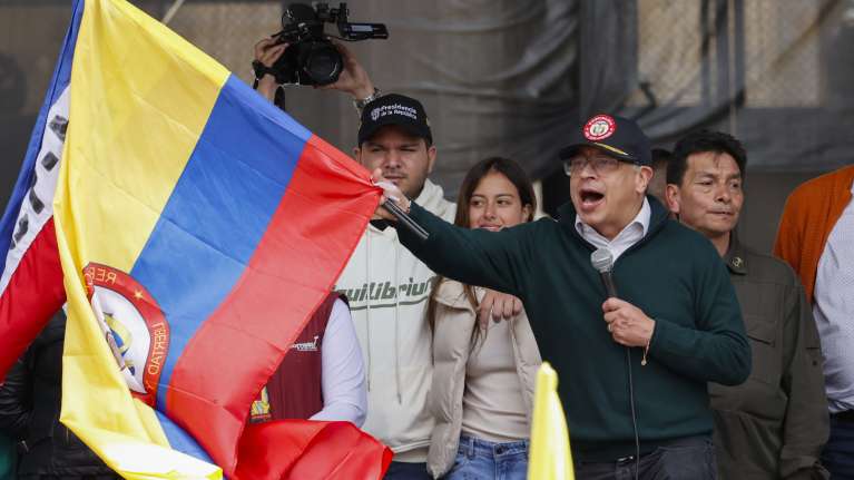 Kolumbian presidentti Gustavo Petro puhuu mikrofoniin ja heiluttaa Kolumbian lippua.