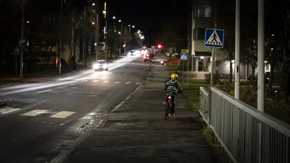 Pyöräilijä ja autoliikennettä öisellä kadulla. 