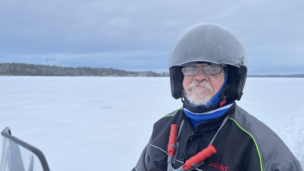 Mönkijän selässä istuva Pekka Tyllilä katsoo kohti kameraa. Taustalla näkyy jäätynyt järvimaisema.
