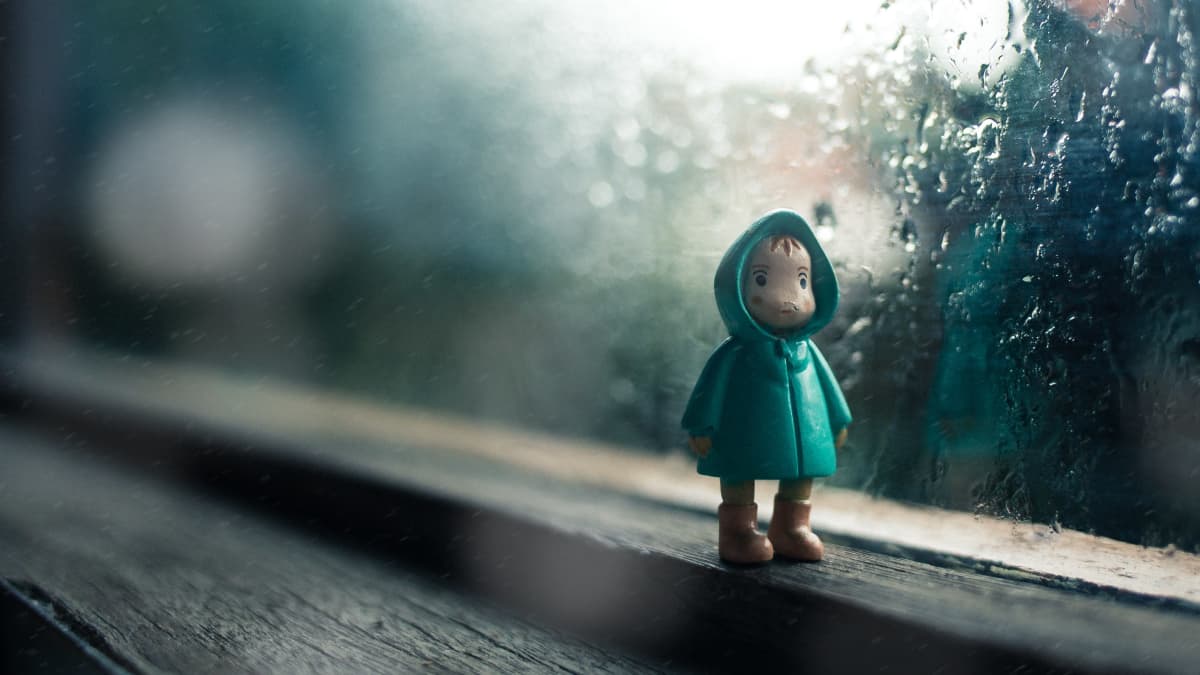 En modellfigur står på ett fönsterbräde med regn på fönstret i bakgrunden.
