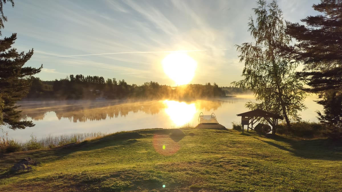 Aurinko paistaa aamu-usvaisen järven yllä.