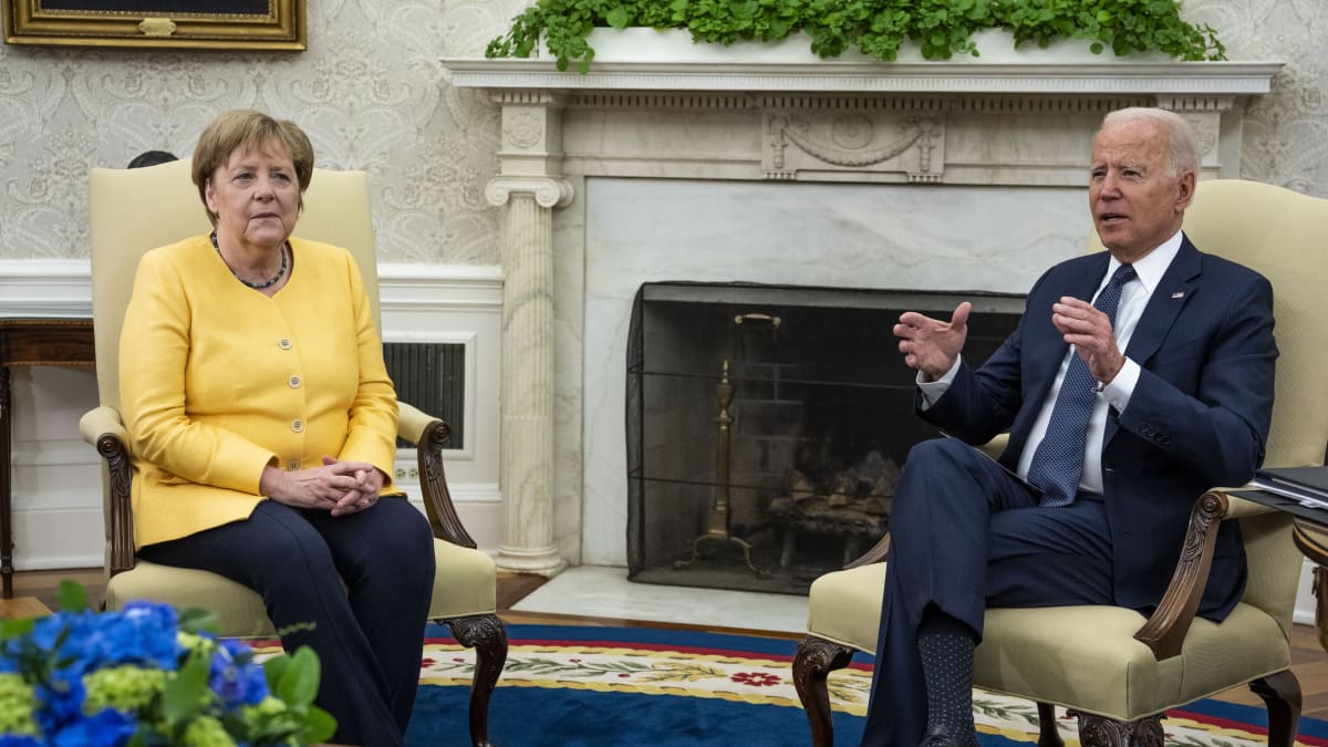 Angela Merkel ja Joe Biden istuvat Valkoisessa talossa. Merkelillä on keltainen jakku ja hieman synkkä ilme. 
