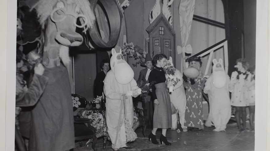 Mustavalkoinen vanha valokuva, jossa teatterin näyttämöllä on esityksen tekijöitä muumi-asuissa ja juhlavissa asuissa esityksen jälkeen.