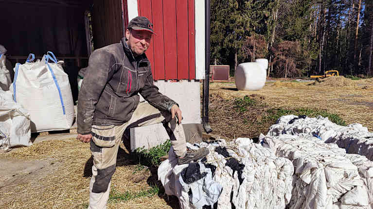 Man står med ena benet på marken och det andra benet lutar på pressade plastbalar.
