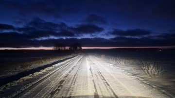 Talviaamu Pöytyällä. Tie halkoo peltomaisemaa auton valoissa, aamu sarastaa. 
