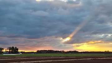 Auringonsäteet tunkeutuvat dramaattisten pilvien välistä maaseudun iltataivaalla.