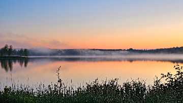 Järvimaisema auringonlaskun aikaan, sumu verhoutuu hiljalleen vedenpintaan.