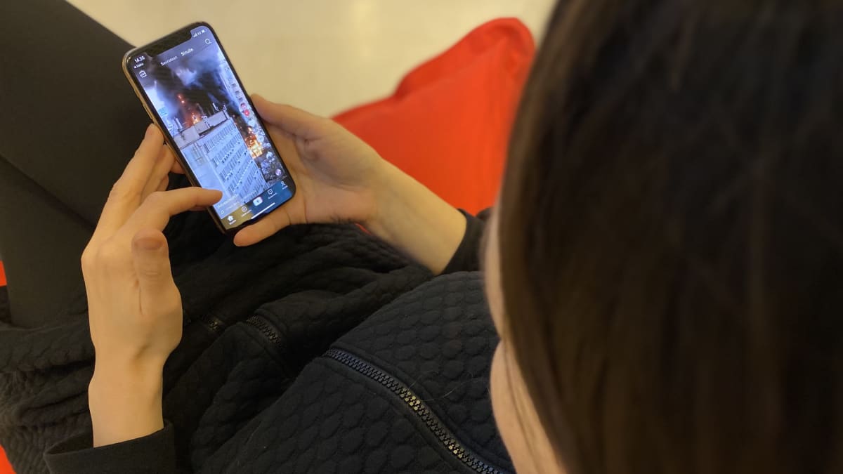 Henkilö selaa Tiktokia. Ruudulla näkyy kerrostaloja ja iso räjähdys.