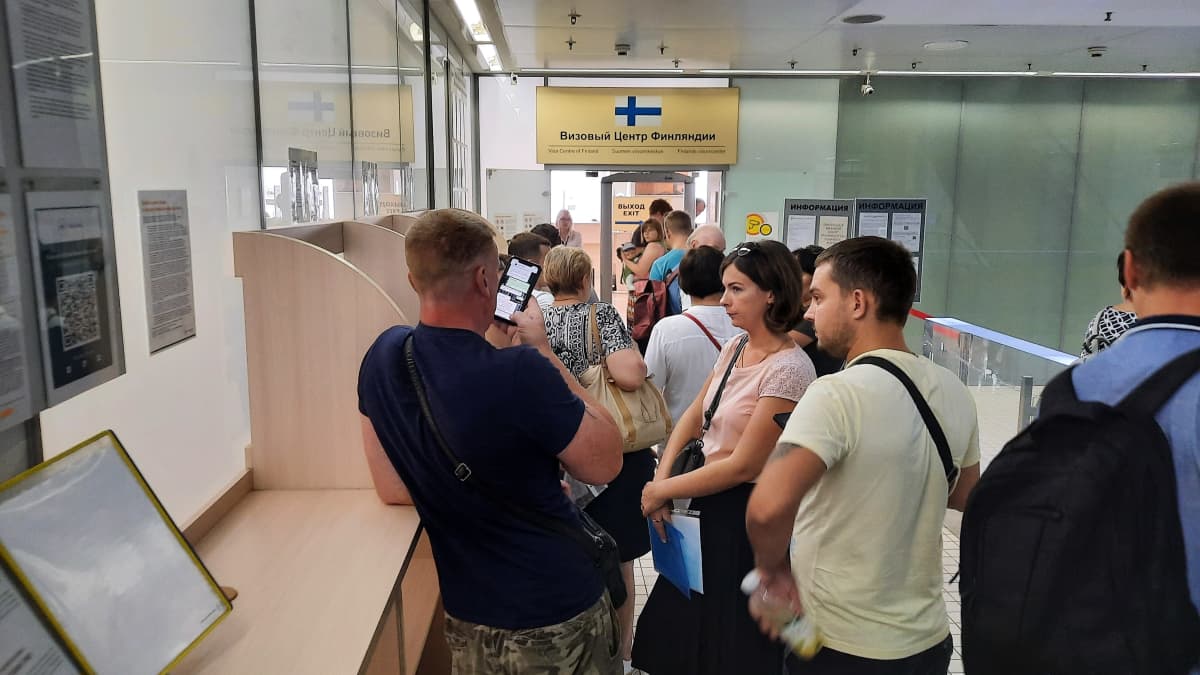 Väkijoukko jonottaa Suomen viisumikeskukseen. Etualalla mies lukee kännykkäänsä.